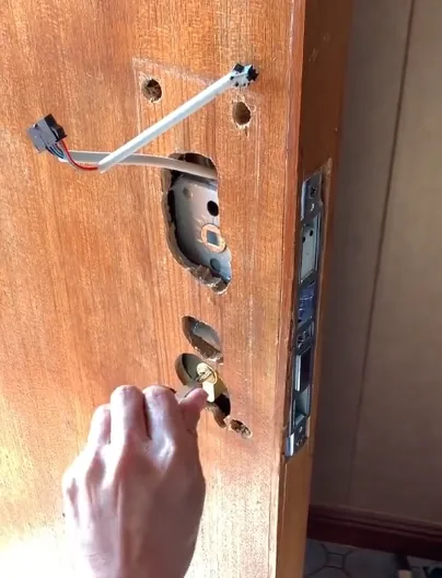 传统面板锁开孔对房门破坏的实拍：木门上开有中央锁体大孔（可看到锁芯内部金属件）、周围分布多个小固定孔（锁体安装孔）、顶部还有线材穿孔与外露线束，门体完整性被显著破坏